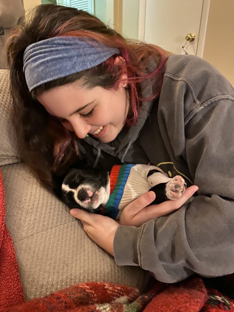 Woman with headband holding a puppy wearing a sweater.